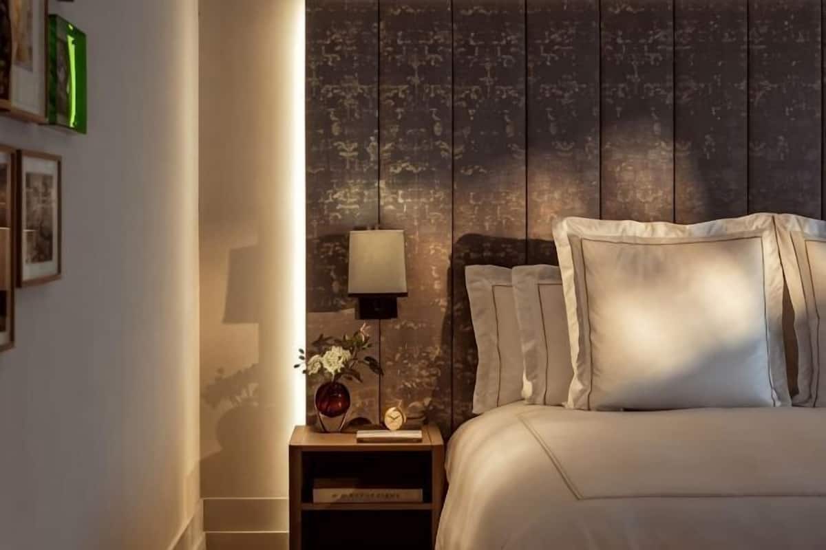 A bedroom with a bed, a bedside table with a lamp, and a wall with a textured pattern.