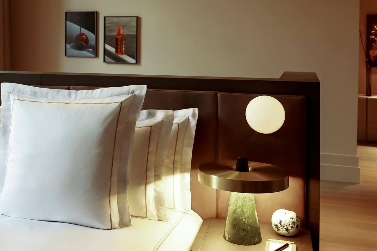 A modern bedroom with a bed, a bedside table with a lamp, and artwork on the wall.