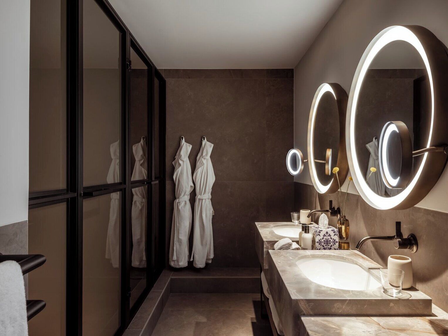 A modern bathroom with two sinks, a large mirror with lighting, and a glass-enclosed shower area.