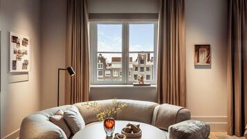 Een moderne woonkamer met een ronde tafel, een beige bank en uitzicht op gebouwen door een raam.