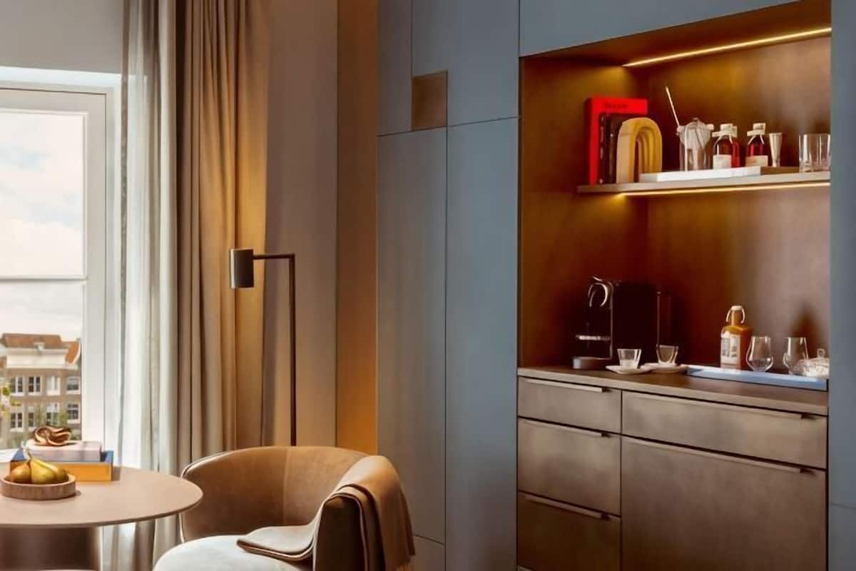 Une chambre dâhĂŽtel moderne avec une table ronde, une chaise, un canapĂ©, un bureau avec une lampe et une Ă©tagĂšre contenant divers objets.