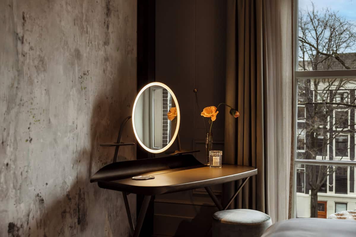 A room with a desk, a round mirror, and a vase with flowers.