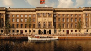 Un grande edificio storico con un fiume di fronte, con una barca ormeggiata sulla riva.
