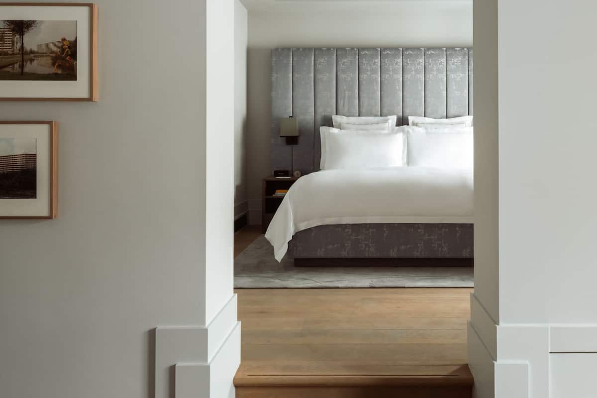 A modern bedroom with a large bed, a grey headboard, and a nightstand with a lamp.