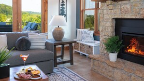 Una sala de estar acogedora con chimenea, un sofá, una mesa de centro con aperitivos y vistas al exterior.