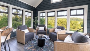 Una sala de estar con paredes de madera oscura, ventanas amplias, muebles de mimbre y una mesa para jugar al ajedrez.