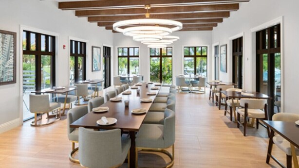Un comedor amplio con mesas y sillas largas, ventanas grandes y un diseño de techo moderno.