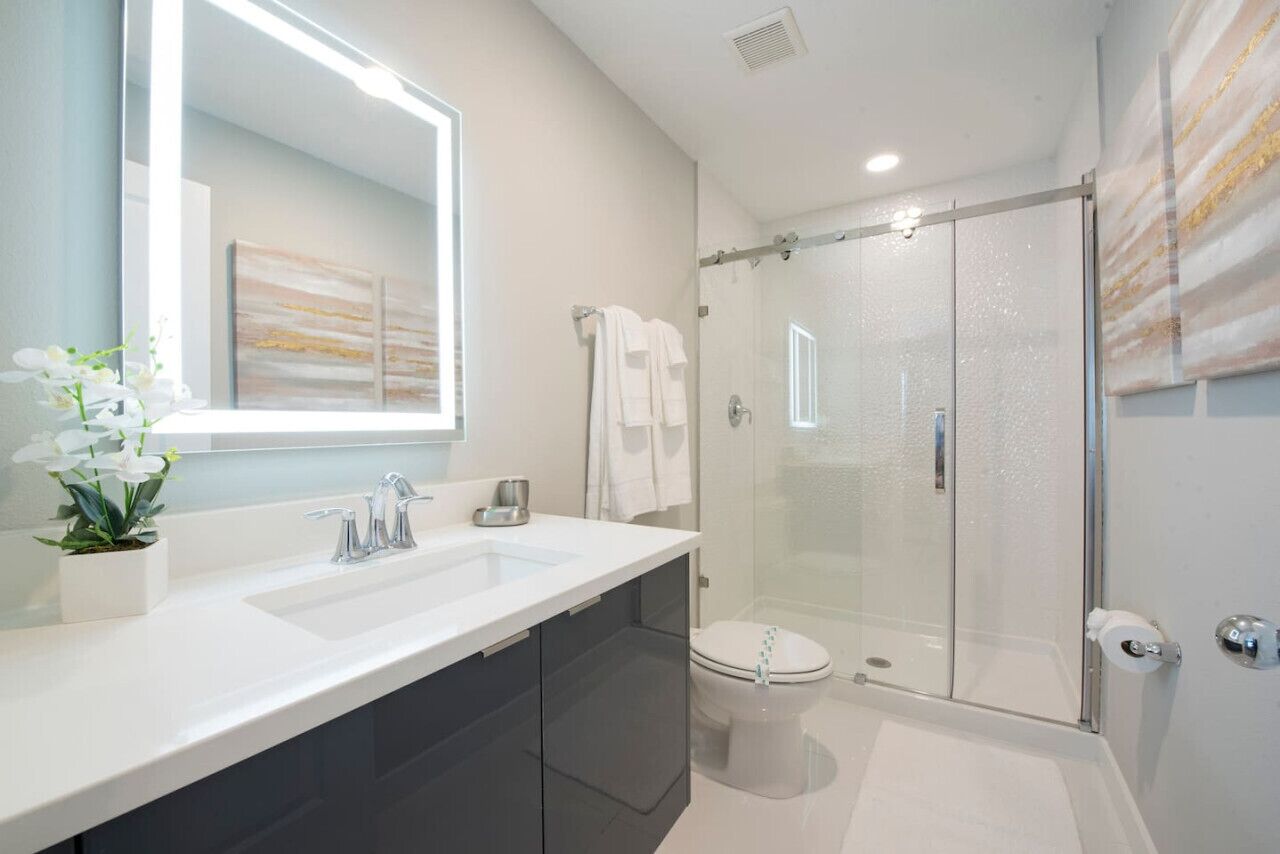 A modern bathroom with a white sink, dark cabinets, a glass shower enclosure, and a toilet.
