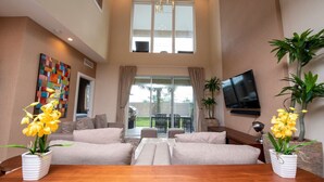 A spacious living room with a large window, a flat-screen TV, and two potted yellow orchids. - 4BD luxury All suites home with BBQ near Disney (Kissimmee)