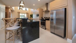A modern kitchen with a central island, stainless steel appliances, and a hanging light fixture.