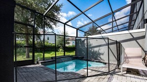 A swimming pool with a glass enclosure, surrounded by a brick patio. - Incredible 4BD home with Pool and BBQ near Disney (Kissimmee)