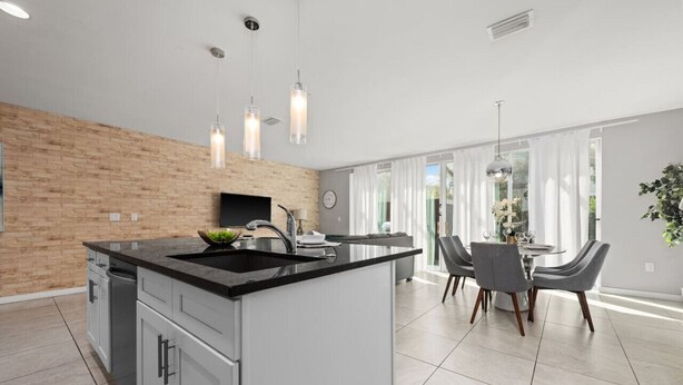 A modern kitchen with a central island, grey cabinetry, and pendant lighting. - Incredible 4BD home with Pool and BBQ near Disney (Kissimmee)
