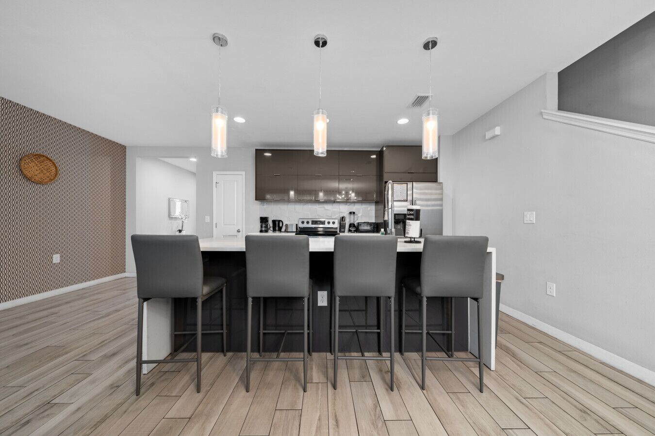A modern kitchen with a central island, bar stools, pendant lighting, and a patterned backsplash.