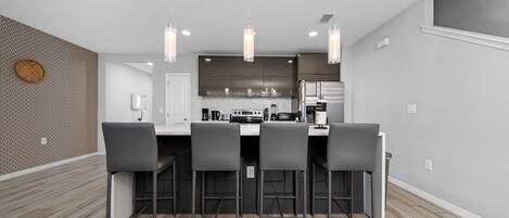 Una cocina moderna con una isla central, taburetes de bar, iluminación colgante y un salpicadero decorativo.