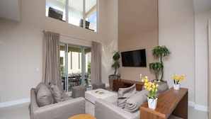 Un salon moderne comprenant un ensemble de canapés, une table basse, un téléviseur fixé au mur et un balcon agrémenté de rideaux.