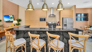Une cuisine moderne dotée d’un grand îlot central, de chaises en bois et de luminaires suspendus.