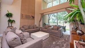 Una sala de estar moderna con techo alto, ventanas amplias y vistas al exterior.