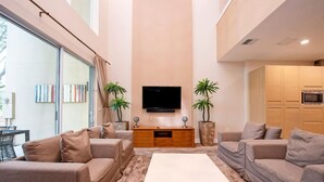 Una sala moderna con un televisor grande, sofás, una mesa de centro y plantas en macetas.