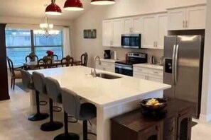 A modern kitchen with a large island, bar stools, and a refrigerator.