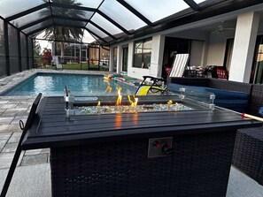 An outdoor pool area with a glass-enclosed patio, a fire feature, and outdoor furniture. - Coral Vista-Tesla Charger 3 Br  w Pool Canal (Cape Coral)