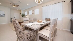 Un coin repas avec une longue table dressée pour quatre personnes, entourée de chaises en osier dotées de coussins.