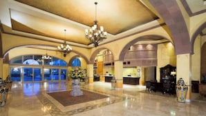 A spacious lobby with a high ceiling, chandeliers, and a reception desk. - Spectacular 2BD Beachfront Condo in Villa del Arco
 (Cabo San Lucas)