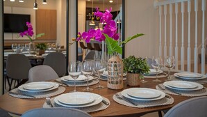 Een eettafel gedekt met borden, glazen en een bloemstuk van paarse orchideeën.
