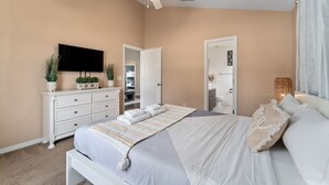 Un dormitorio con una cama, televisión, ventilador de techo y una puerta que da a un baño.
