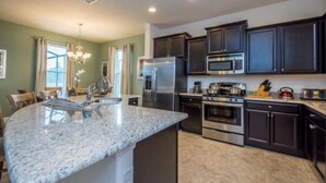 Una cocina moderna con encimeras de granito, electrodomésticos de acero inoxidable y muebles oscuros.