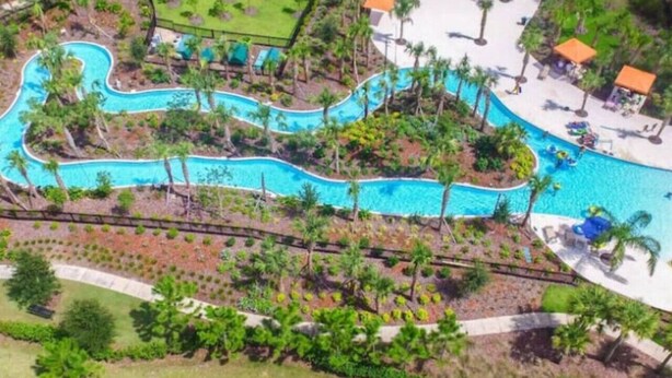 Vista aérea de un complejo turístico con piscina sinuosa, palmeras y tumbonas.