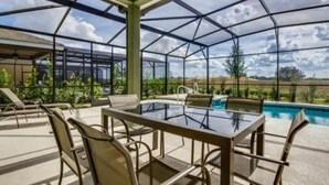 Un espacio al aire libre techado con una mesa y sillas de vidrio, una piscina y vistas al paisaje.