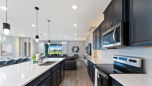 A modern kitchen with dark cabinets, a large island, and a view to the outdoors. - 8BD InstaWorthy home with Pool and Spa near Disney (Davenport)
