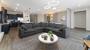 A modern living room with a sectional sofa, a round coffee table, and a kitchen area in the background. - 8BD InstaWorthy home with Pool and Spa near Disney (Davenport)