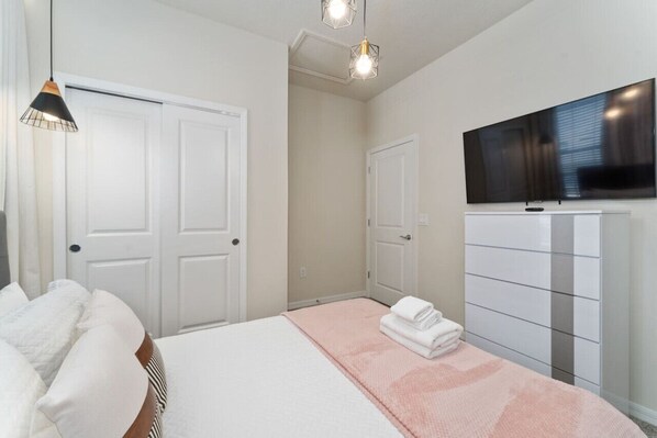 A bedroom with a bed, a dresser, a television, and two pendant lights.