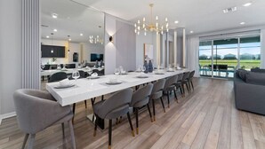 A modern dining area with a long table, grey chairs, and a chandelier. - 8BD InstaWorthy home with Pool and Spa near Disney (Davenport)