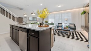 A modern kitchen with a central island, pendant lighting, and a dining area with a black and white rug.
