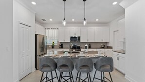 Uma cozinha moderna com armários brancos, eletrodomésticos de aço inoxidável e uma ilha central com banquetas.