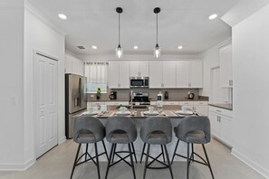 A modern kitchen with white cabinets, stainless steel appliances, and a central island with bar stools. - 4BD Paradise Home Sleeps 13 with Pool Spa and BBQ (Davenport)
