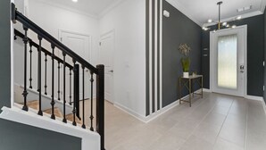 Um corredor moderno com escadas, uma porta de vidro jateado e uma pequena mesa com uma planta.