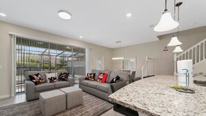 A modern kitchen with granite countertops, a dining area with a grey sofa and ottoman, and a large sliding glass door leading to a balcony. - 5BD Sleeps 14 Mickey Home with Arcade Pool and BBQ (Davenport)