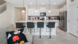 A modern kitchen with white cabinets, a stainless steel refrigerator, and a central island with bar stools. - 5BD Sleeps 14 Mickey Home with Arcade Pool and BBQ (Davenport)