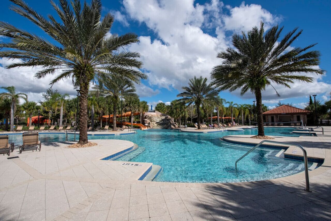 A swimming pool with palm trees, lounge chairs, and a clear sky.