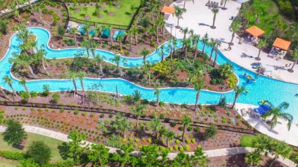 An aerial view of a resort with a winding pool surrounded by palm trees and lounge areas. - 5BD Sleeps 14 Mickey Home with Arcade Pool and BBQ (Davenport)