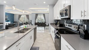 A modern kitchen with stainless steel appliances, a central island, and a dining area with a view. - 6BD InstaWorthy home pool cine and BBQ near Disney (Davenport)
