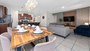 Una cocina moderna con muebles de madera, una mesa de comedor con platos y tazas blancos, y una sala de estar con un sofá gris y un sillón azul.