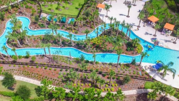 Vista aérea de un complejo turístico con una piscina serpenteante rodeada de palmeras y zonas de descanso.