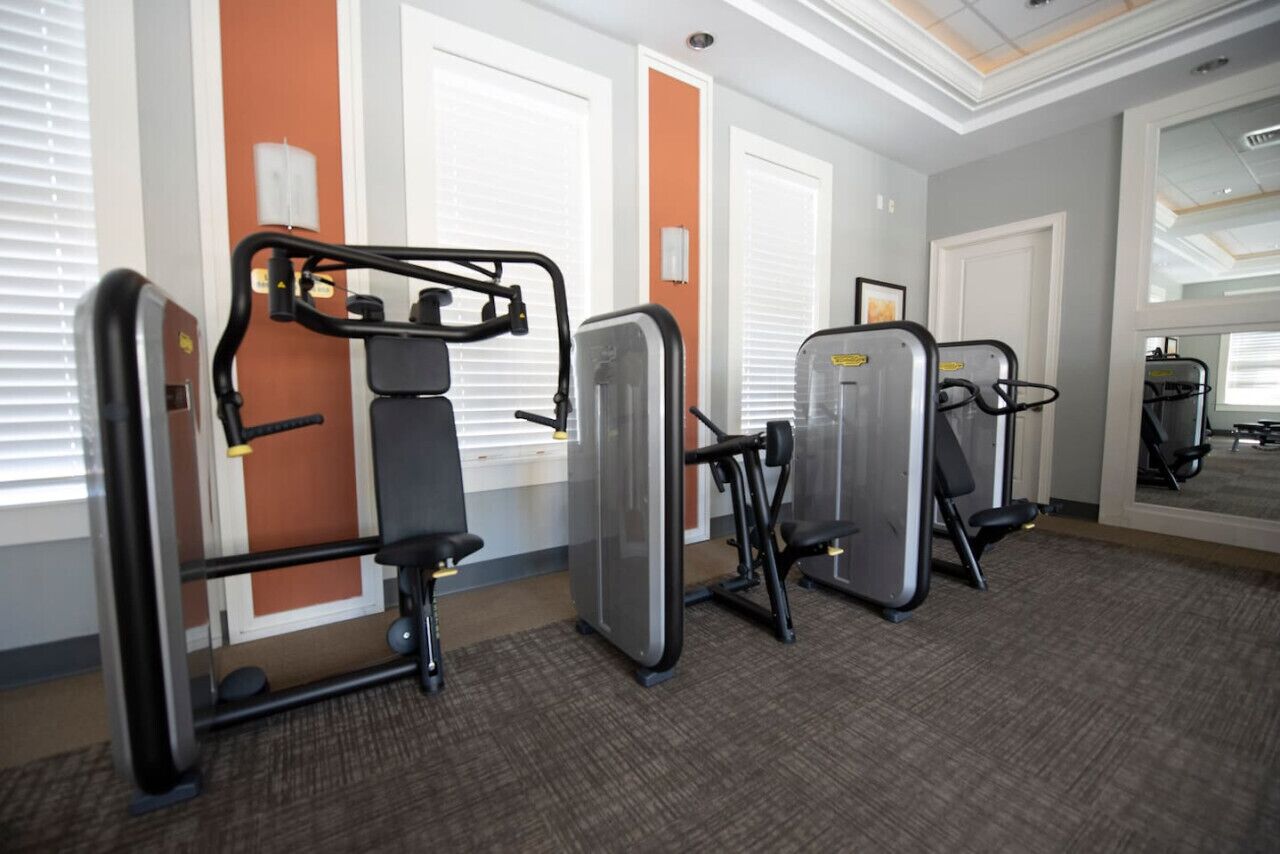 A fitness room with exercise equipment, including a chest press machine, a leg press machine, and a lat pulldown machine.