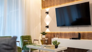 Ein modernes Wohnzimmer mit einem Wand-Fernseher, einem grünen Sessel, einem weißen Konsolentisch und einer Topfpflanze.
