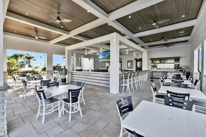 An outdoor dining area with multiple tables and chairs, a bar area, and a view of the outdoors.