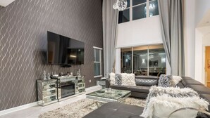 Una sala de estar moderna con una televisión de pantalla plana, una mesa de centro de vidrio, un sofá y una chimenea.